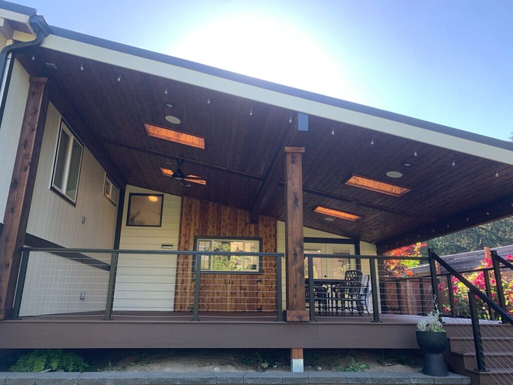 Covered outdoor living room with wood ceiling, skylights, string lights, and cable railing in the Pacific Northwest