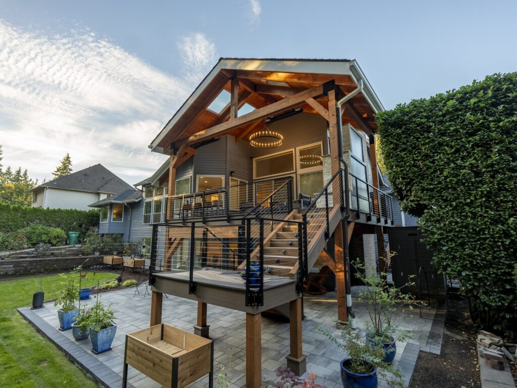 Covered deck with a timber frame gable roof, cable railing and warm lighting, built by Tenhulzen Construction in the Pacific Northwest