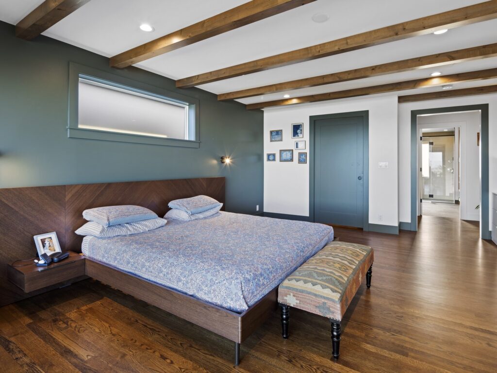 Bedroom with a deep teal painted accent wall, walnut headboard and patterned bedding, painted by Tenhulzen Construction