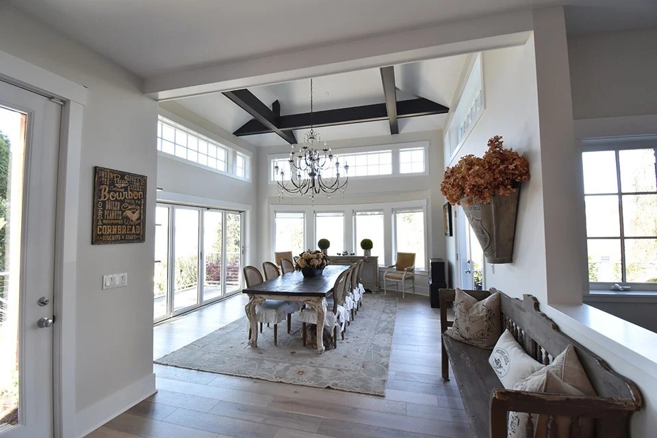 A bright dining room with a long farmhouse table, beamed ceiling and fresh white walls